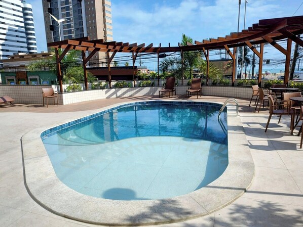 Una piscina con un columpio de madera, sillas de descanso y mesas.
