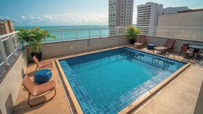 Una piscina en la azotea con vista al océano, rodeada de sillas de descanso y plantas en macetas.