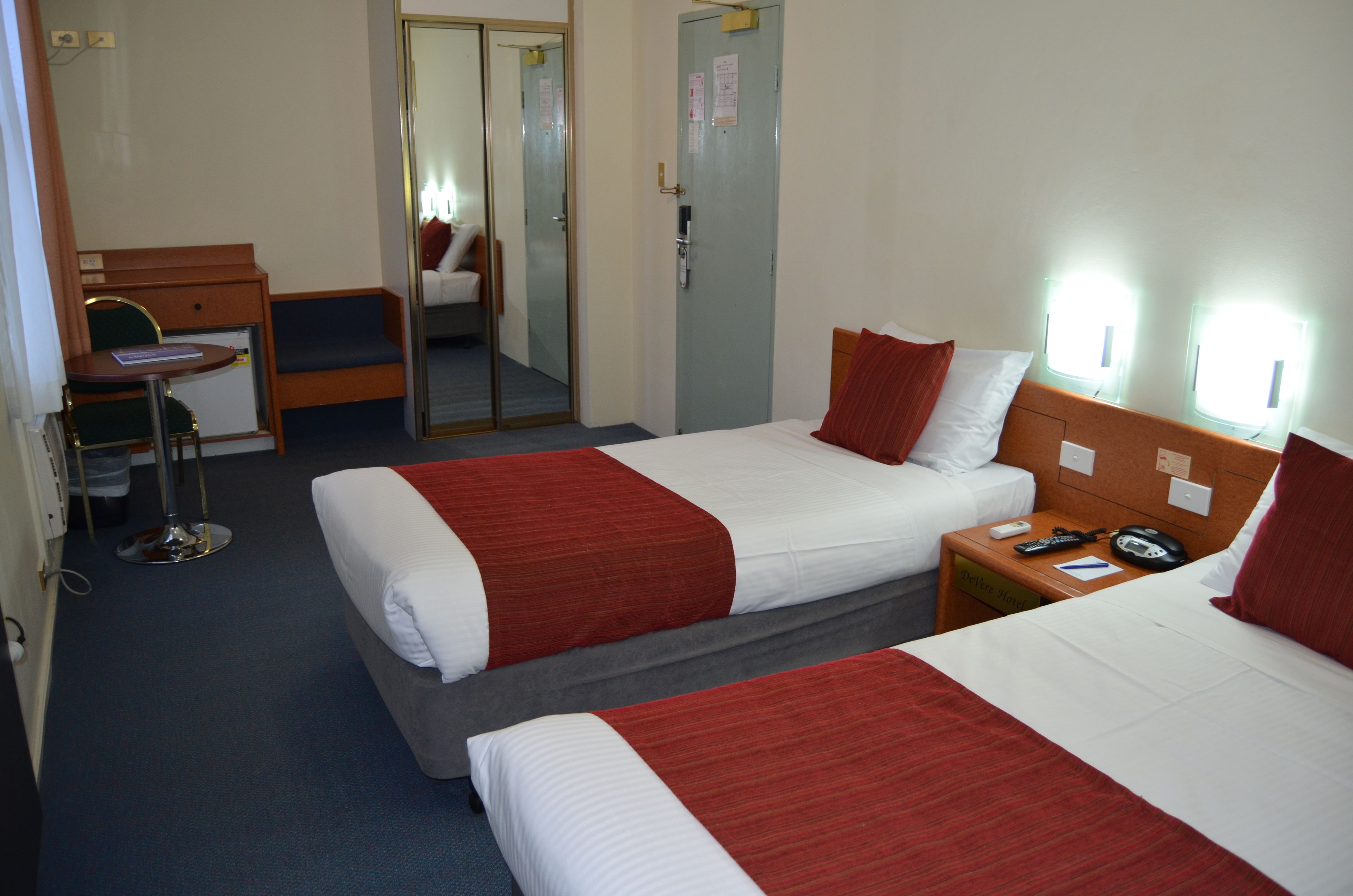 Une chambre d’hôtel avec deux lits, un bureau, une chaise et un miroir.