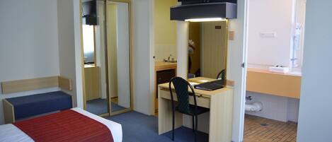 Habitación de hotel con dos camas, un escritorio, una silla, un televisor y un baño visible a través de una puerta abierta.