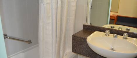 A bathroom with a white bathtub, a shower curtain, a sink with a granite countertop, and a mirror above the sink.