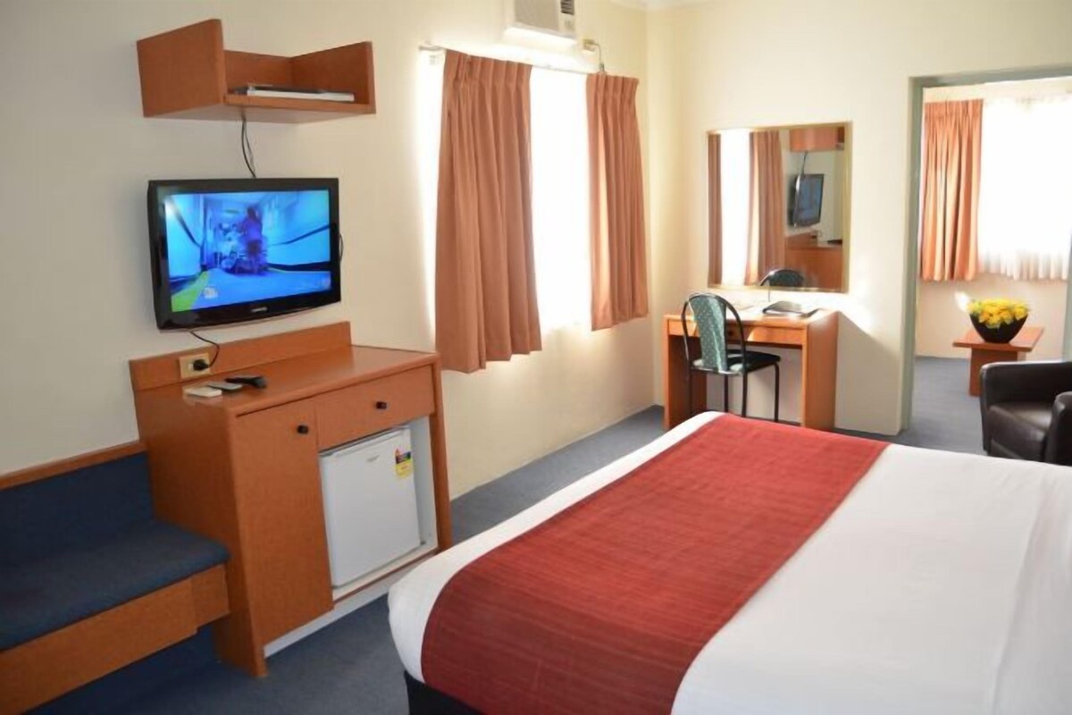 A hotel room with a bed, a desk, a chair, a television, and a small refrigerator.