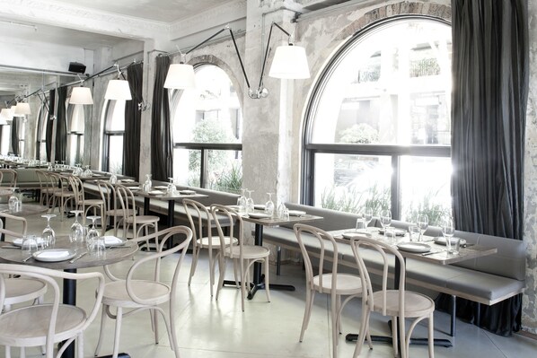 A restaurant with long tables, chairs, and hanging lamps.