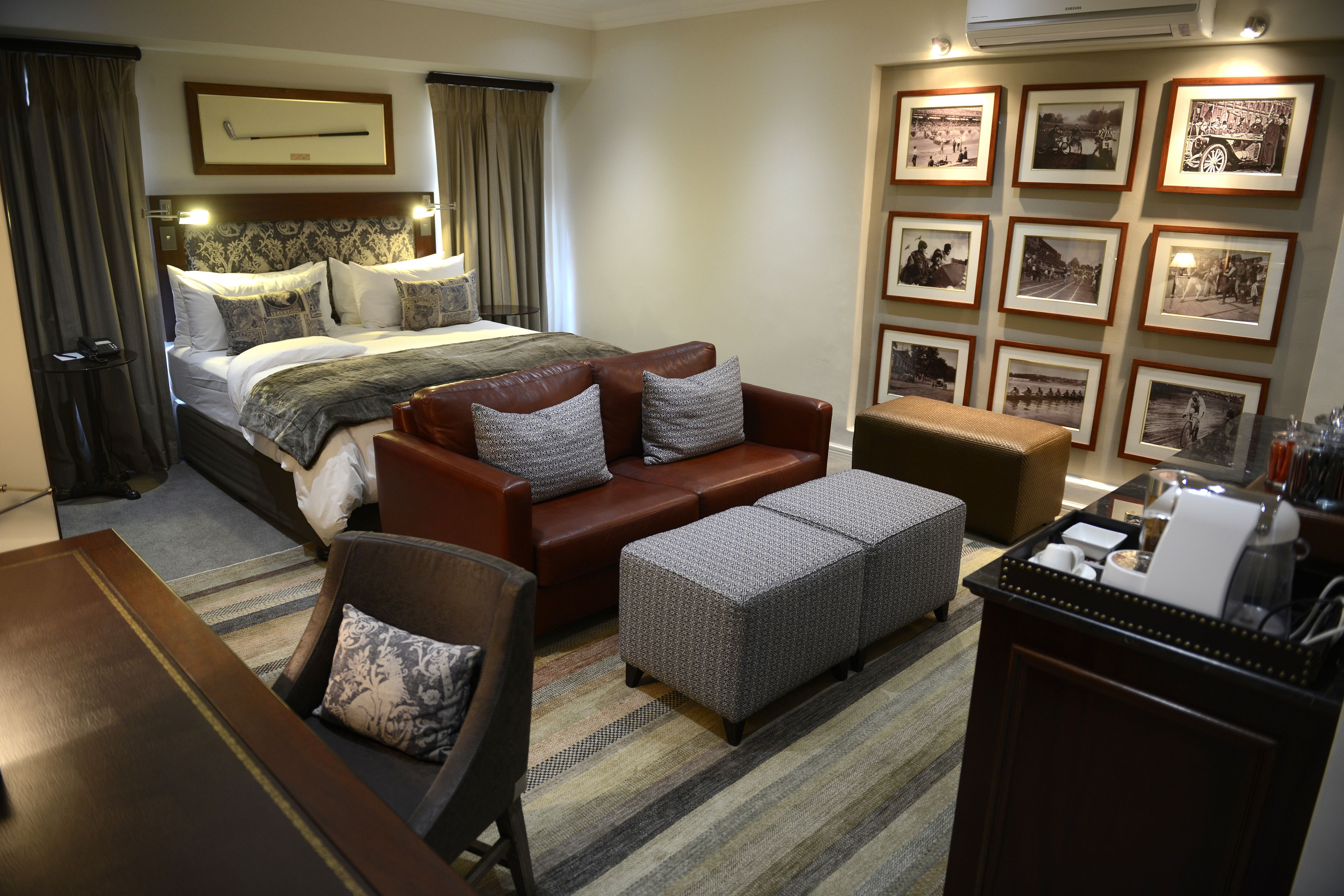 A hotel room with a bed, a sofa, an ottoman, a coffee table, and a wall with framed pictures.