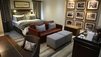 A hotel room with a bed, a sofa, an ottoman, a coffee table, and a wall with framed pictures.