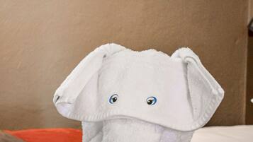 Uma toalha macia em forma de elefante sobre uma cama com cobertura marrom e almofada laranja.