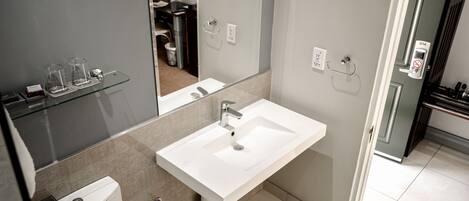 Un baño moderno con un lavamanos blanco, estantes de vidrio y un inodoro.