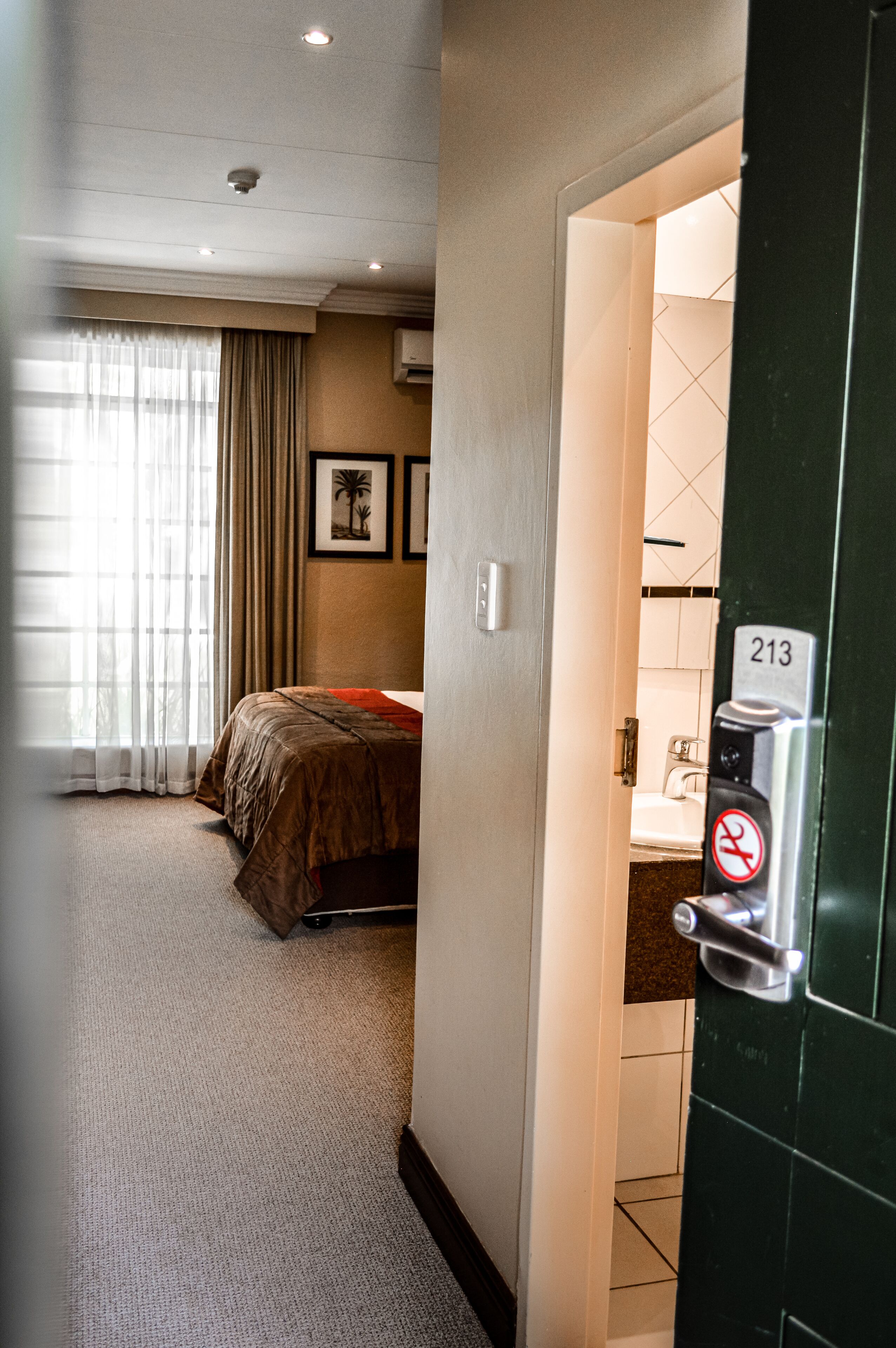 A hotel room with a bed, a bathroom with a sink, and a door with a number lock.