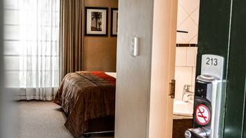 A hotel room with a bed, a bathroom with a sink, and a door with a number lock.