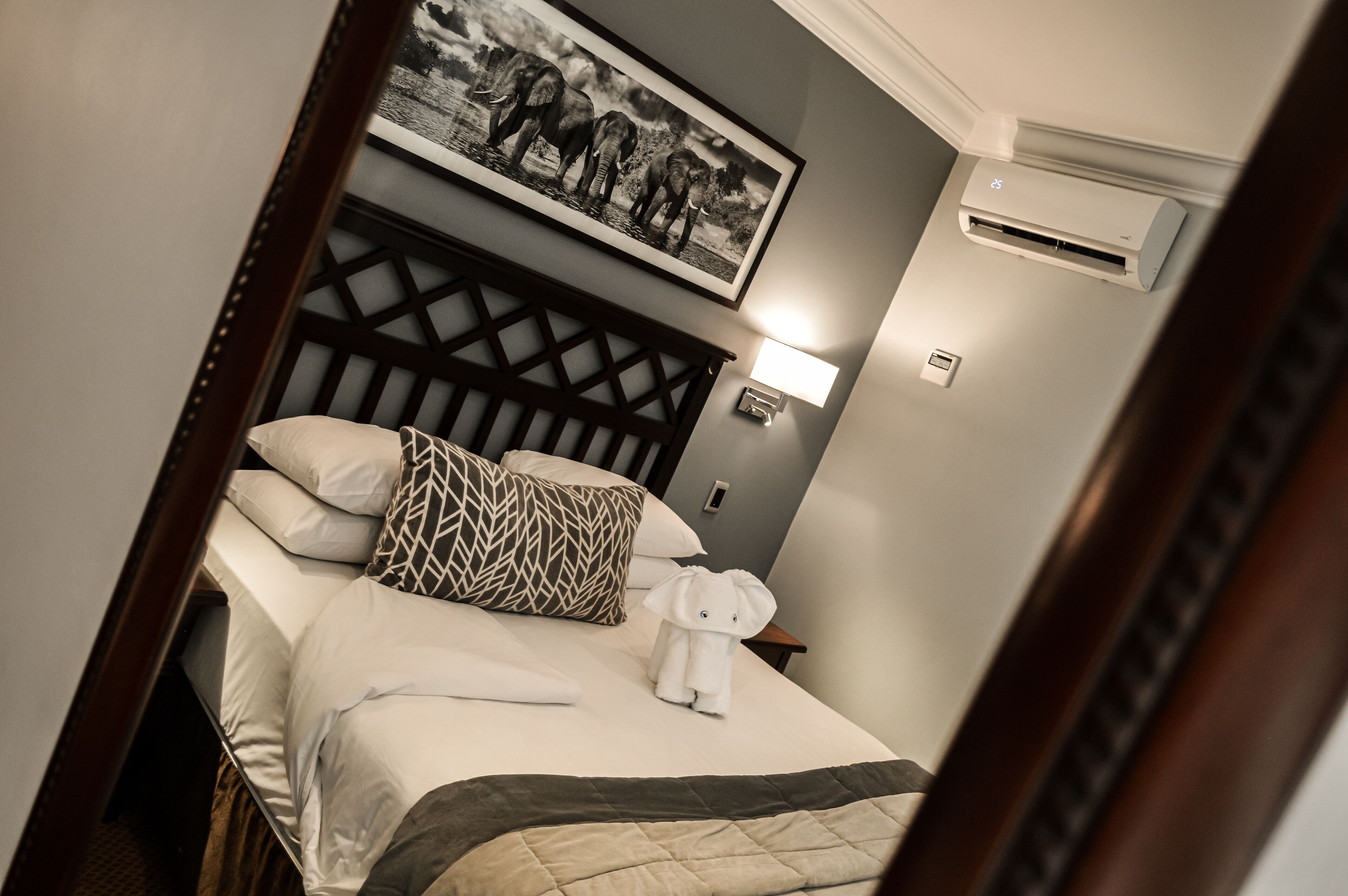 A neatly made bed with a patterned pillow, a framed picture above, and a wall-mounted air conditioner.