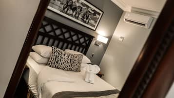 A neatly made bed with a patterned pillow, a framed picture above, and a wall-mounted air conditioner.