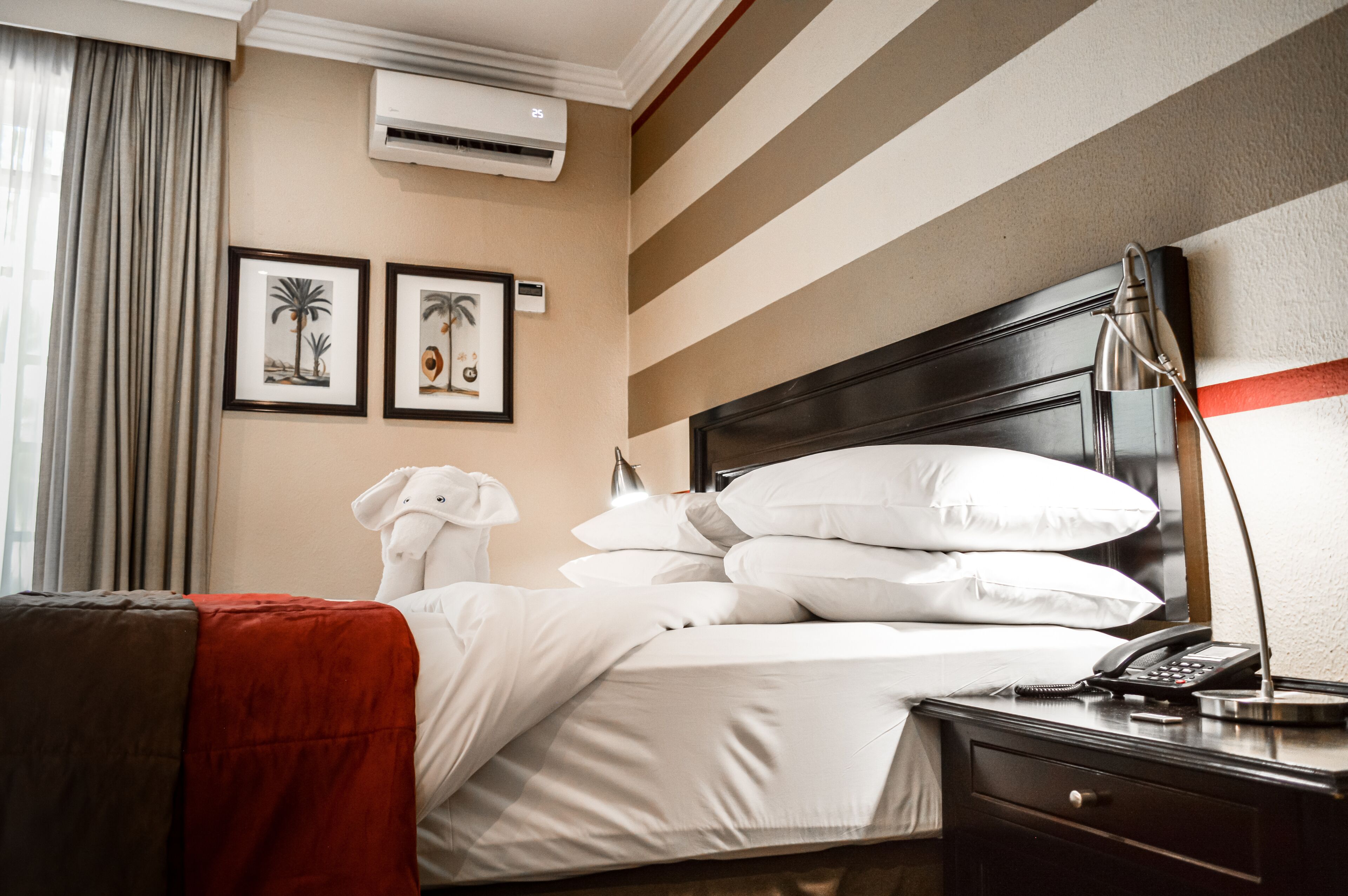 Una habitación de hotel con cama, mesita de noche, lámpara y dos cuadros en la pared.