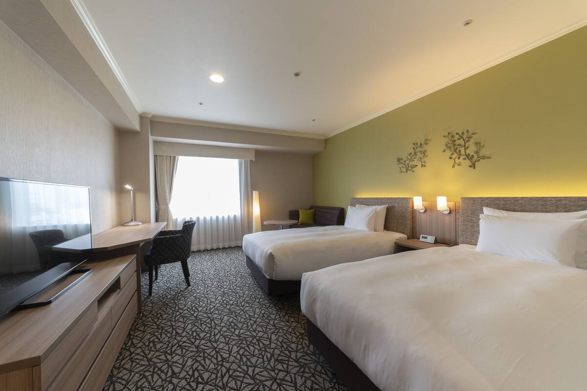 Een hotelkamer met twee bedden, een bureau, een televisie en een raam met gordijnen.