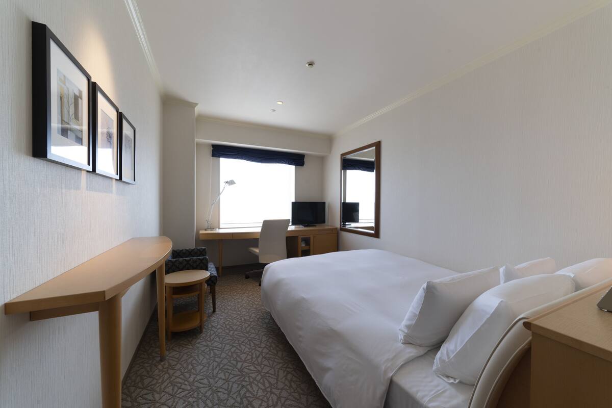 Een hotelkamer met een bed, een bureau, een stoel, een televisie en een raam met gordijnen.