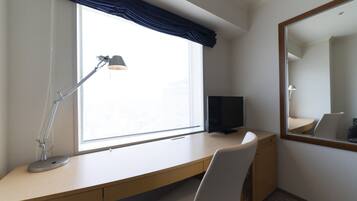 Habitación de hotel con escritorio, silla, televisor, lámpara y un espejo grande.
