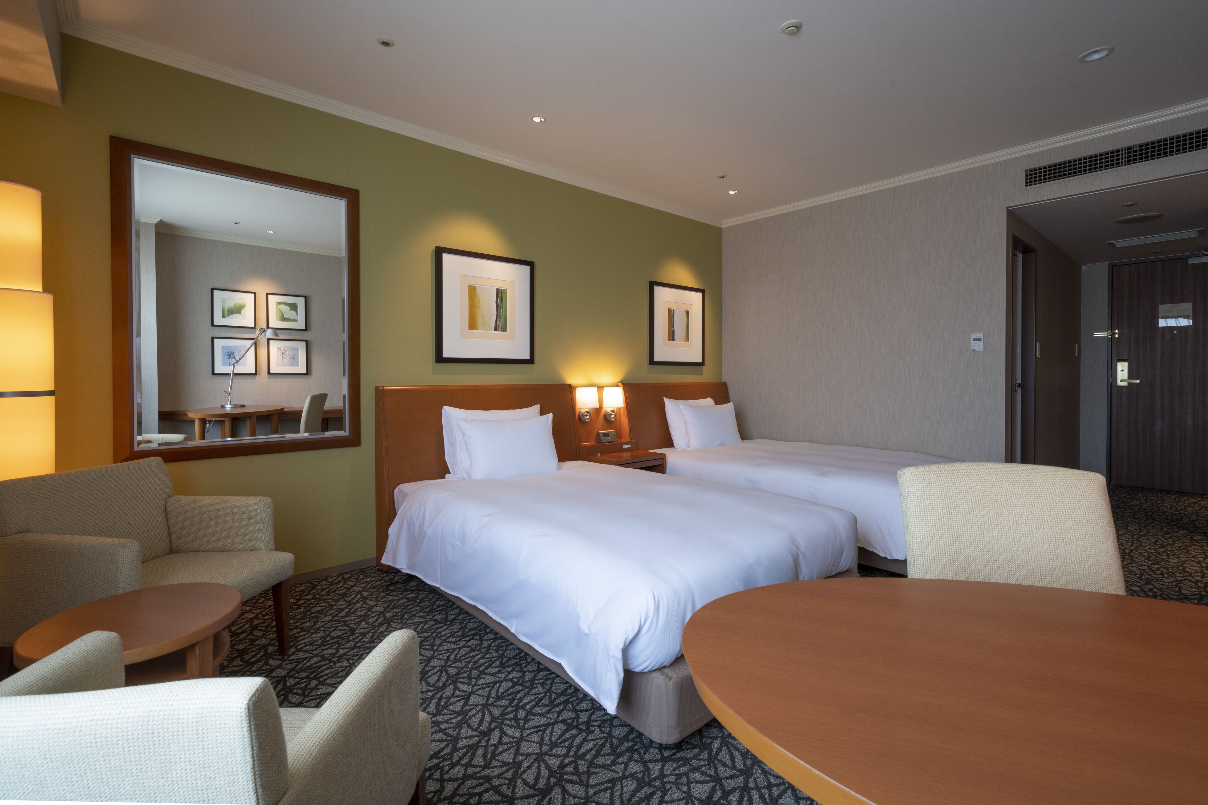 A hotel room with two beds, a sitting area with a table and chairs, and a large mirror.