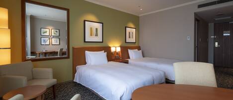 A hotel room with two beds, a sitting area with a table and chairs, and a large mirror.