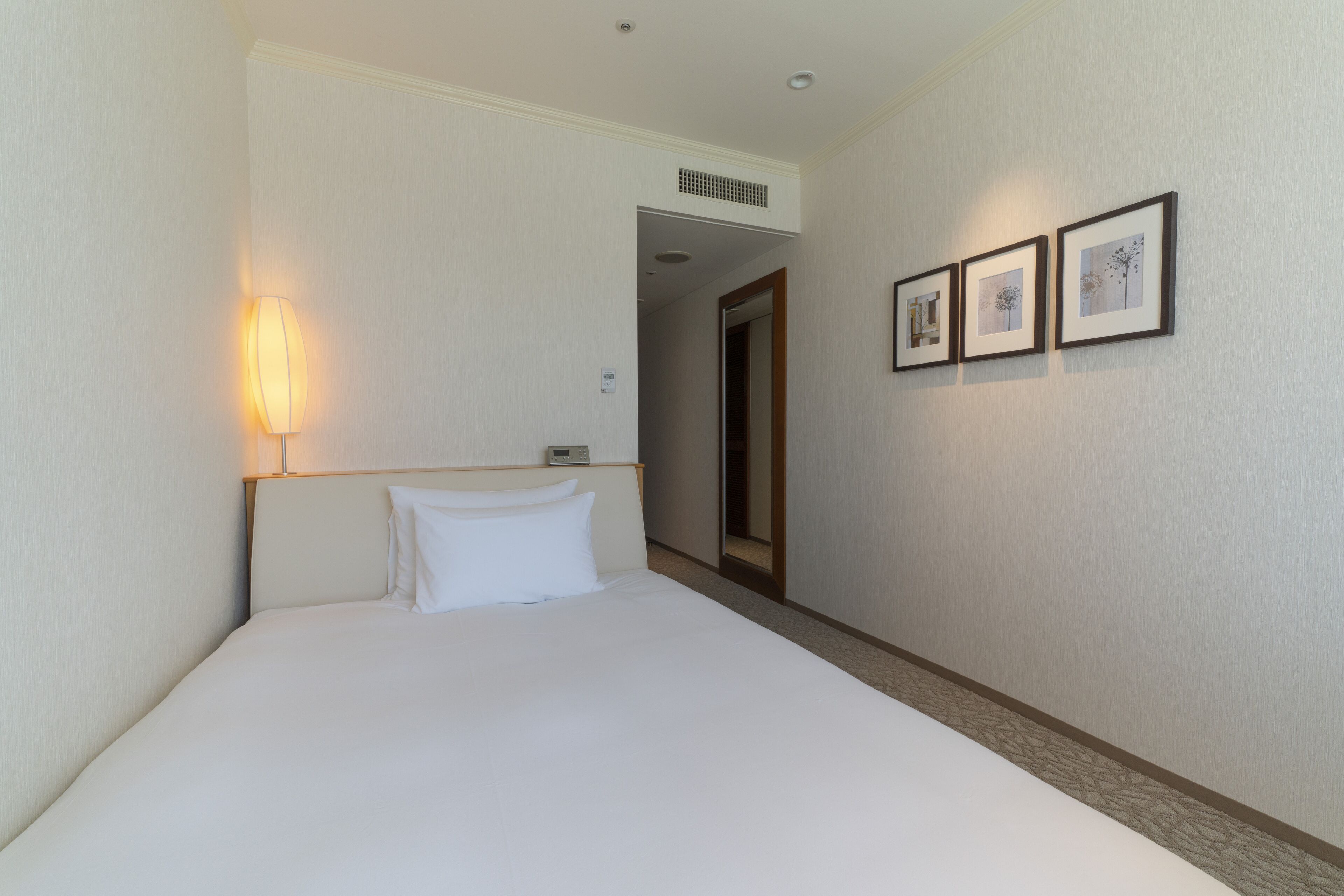 A hotel room with a bed, a nightstand, a wall-mounted lamp, and framed artwork on the wall.