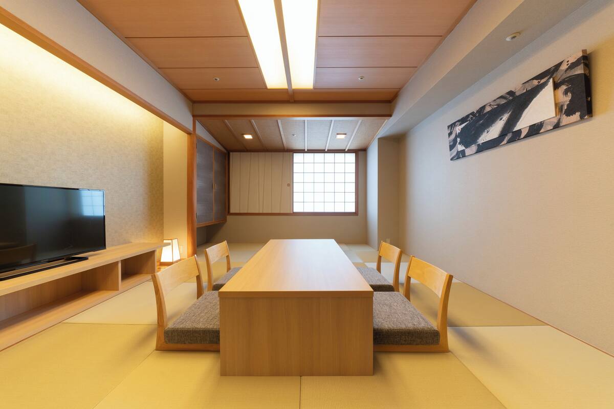 Een moderne vergaderruimte met een lange tafel, stoelen, een flatscreen-tv en een groot raam.