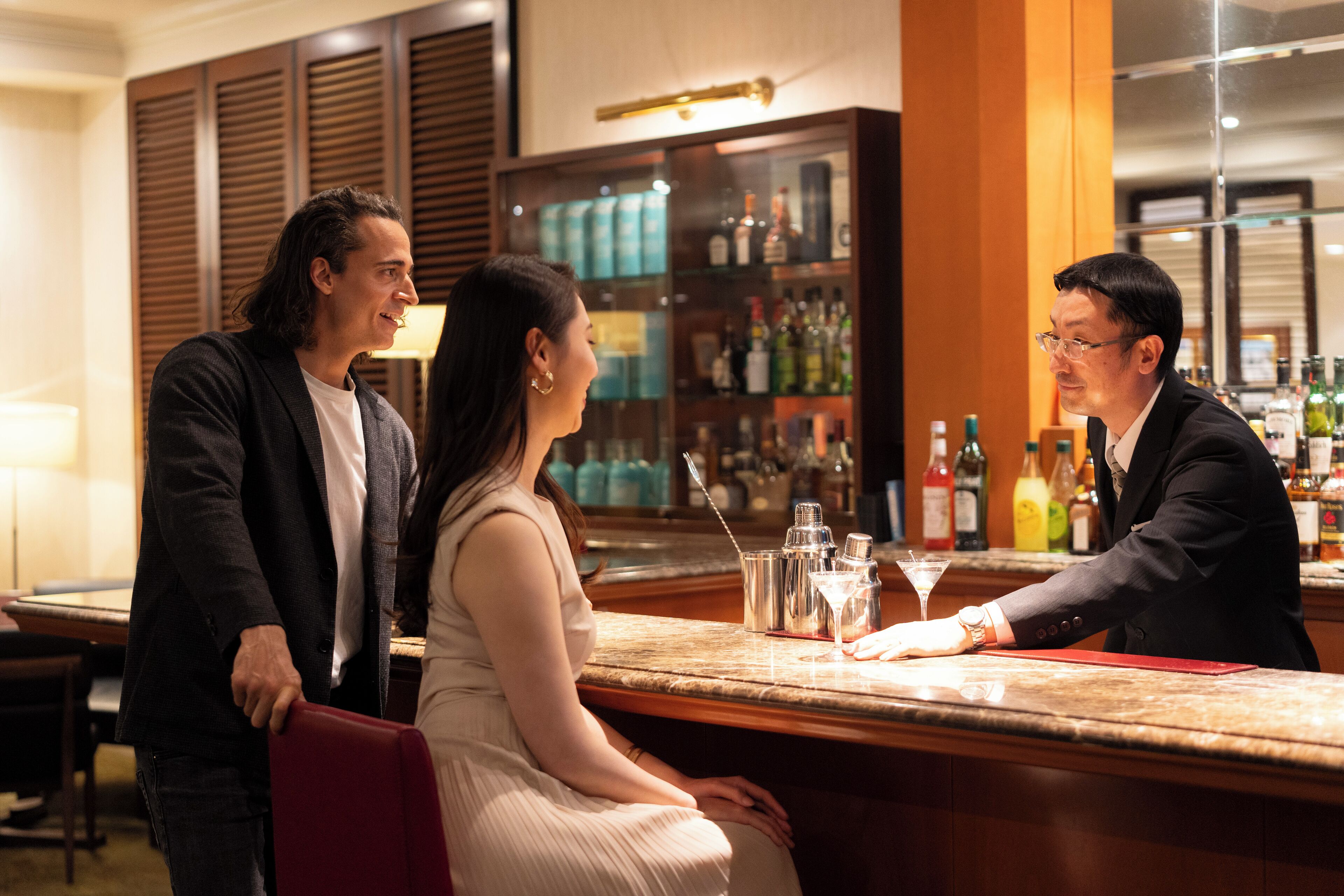 A bar area with a counter, bar stools, and a variety of bottles and glasses.