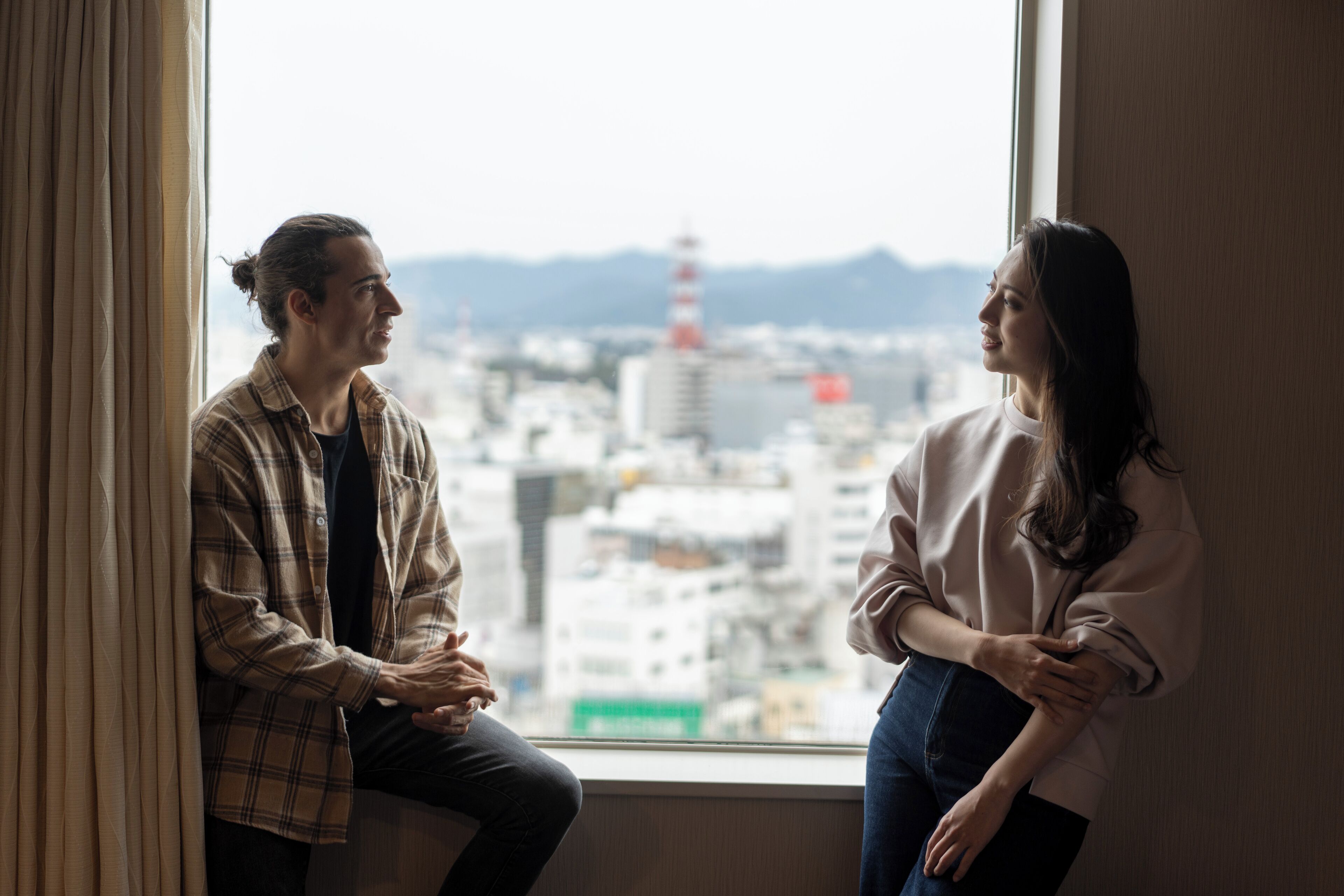 Two people sitting by a window with a cityscape view.