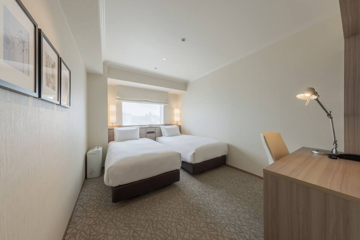 Een hotelkamer met twee bedden, een bureau, een stoel, een lamp en lijstjes met foto's aan de muur.