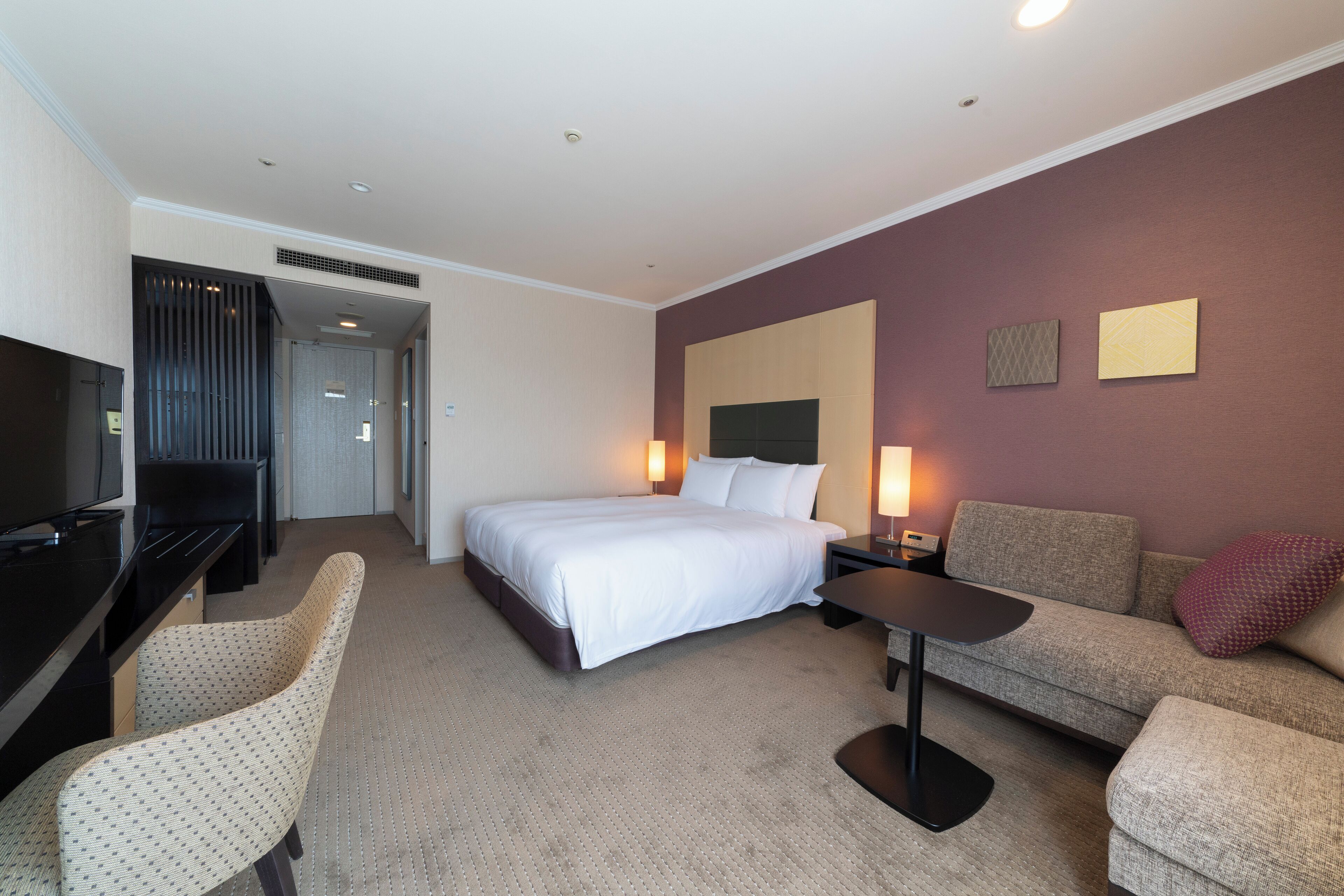 A hotel room with a bed, a desk, a sofa, and a TV.