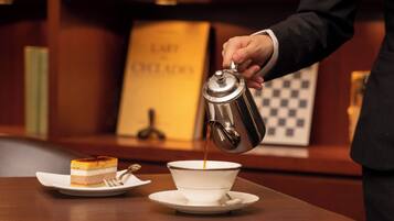 A person pouring coffee into a cup on a table with a slice of cake and a spoon.