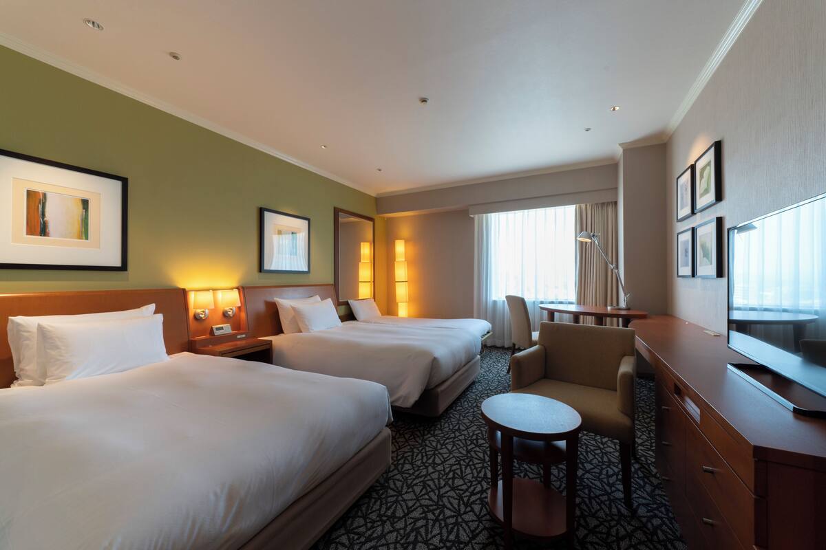 Een hotelkamer met twee bedden, een bureau, een stoel en een televisie.