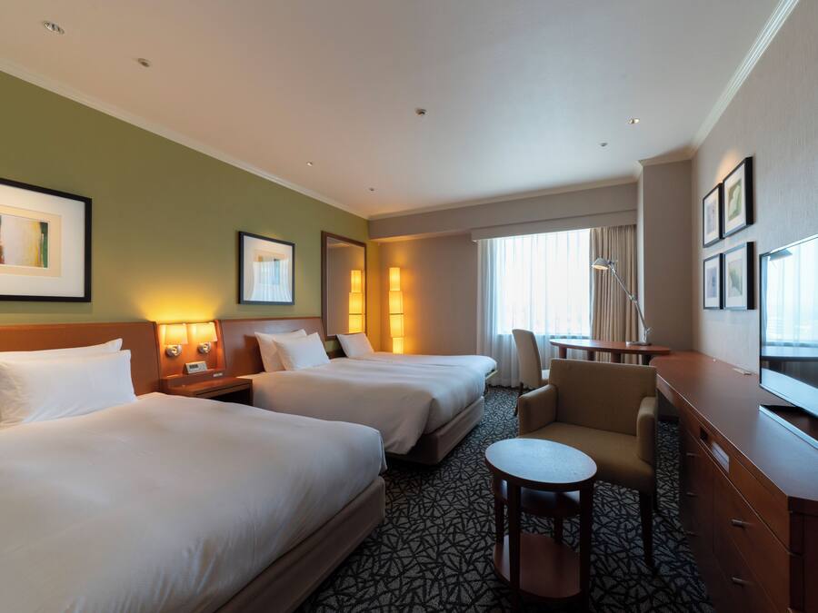 A hotel room with two beds, a desk, a chair, and a television.