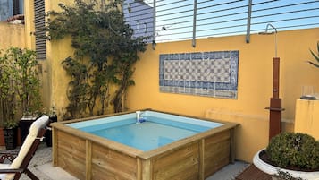 A rectangular wooden pool with a blue interior, surrounded by a stone-tiled patio.