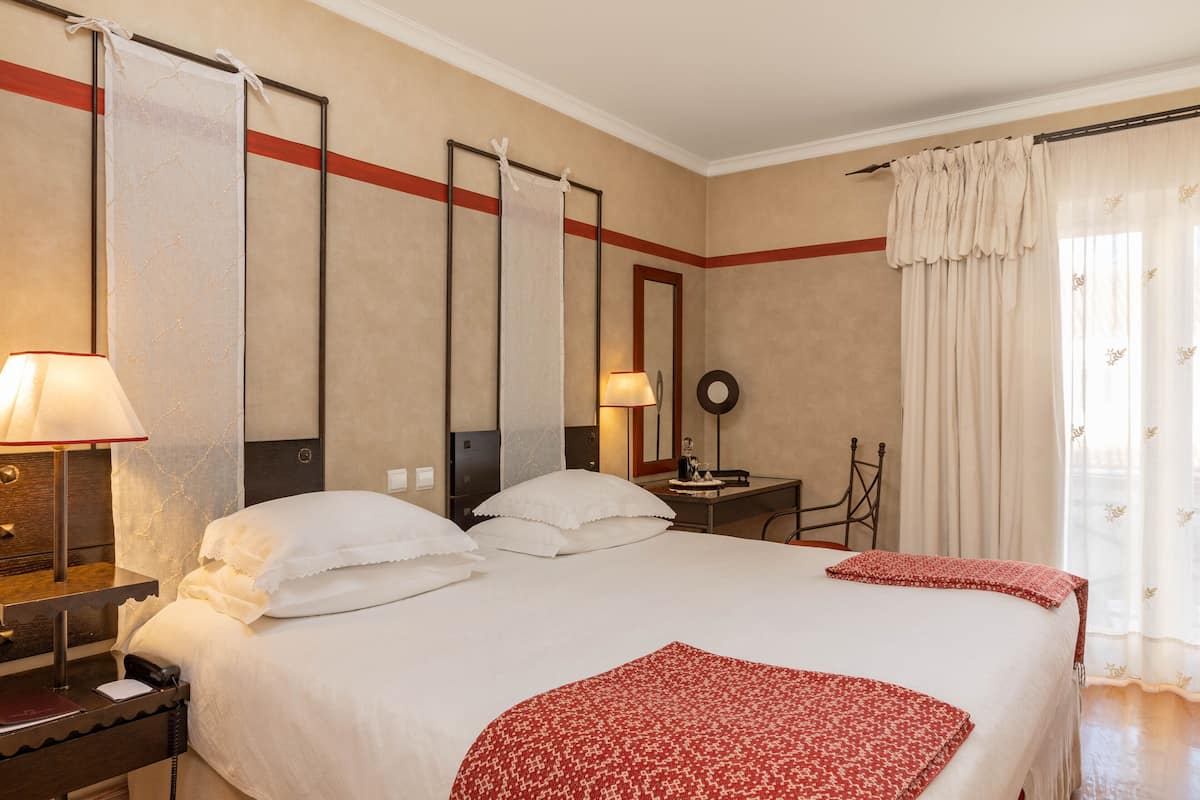 A hotel room with a large bed, a desk, a chair, a telephone, and a mirror.