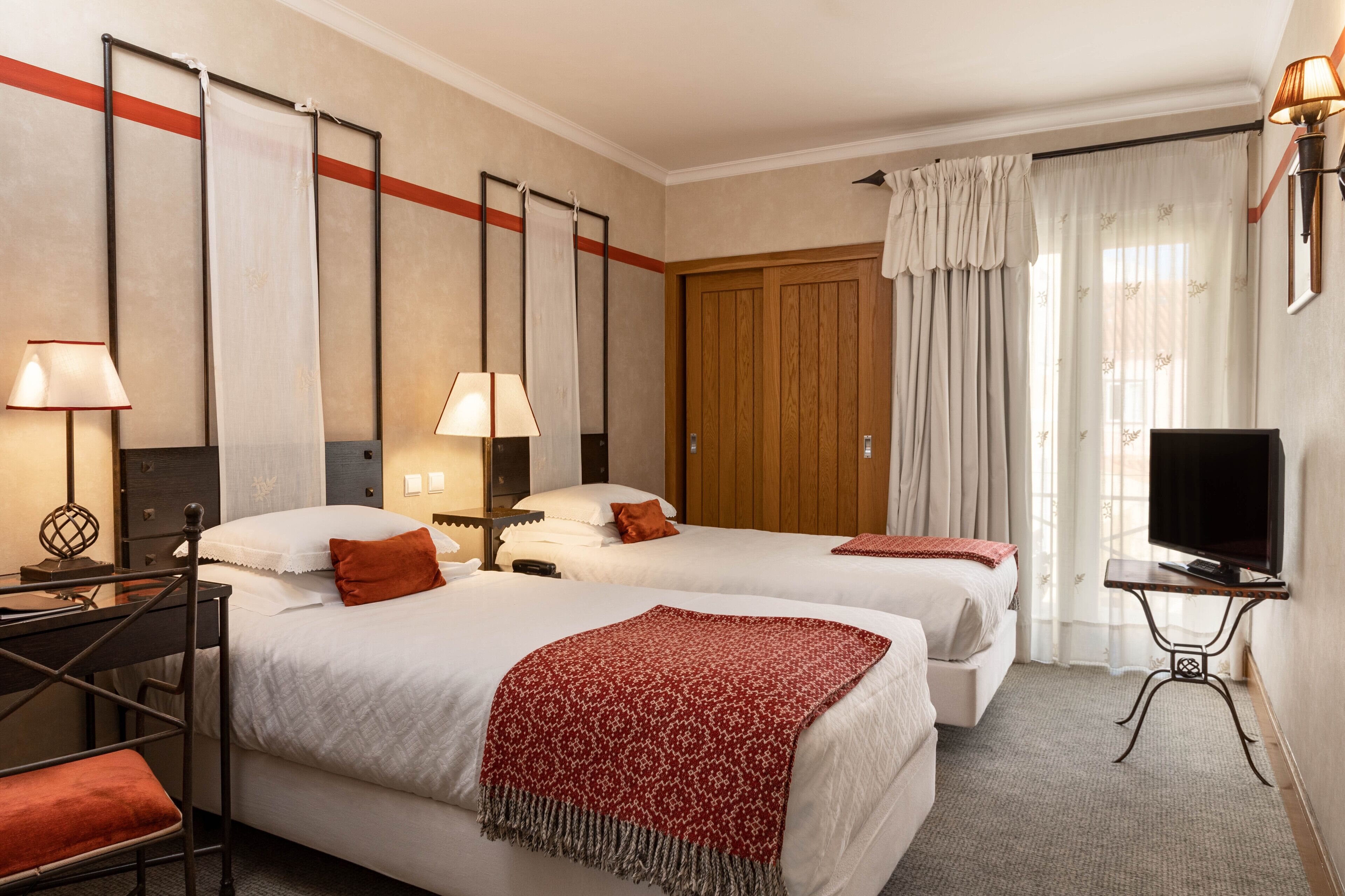 Une chambre d’hôtel avec deux lits, un bureau avec une chaise, une télévision et une armoire.