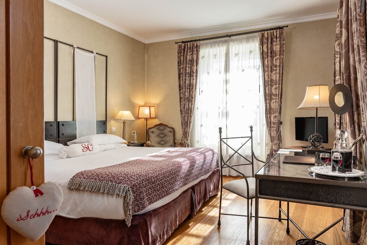 A hotel room with a bed, bedside lamps, a desk with a mirror, and a television.