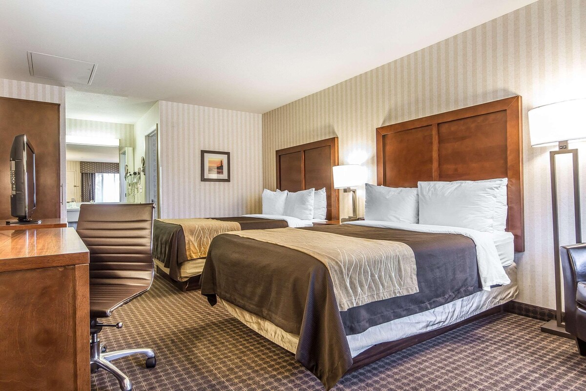 A hotel room with two beds, a desk, and a chair.