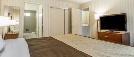 Ein Hotelzimmer mit Bett, Fernseher, Kommode und einem durchgegangenen Tür sichtbaren Badezimmer.