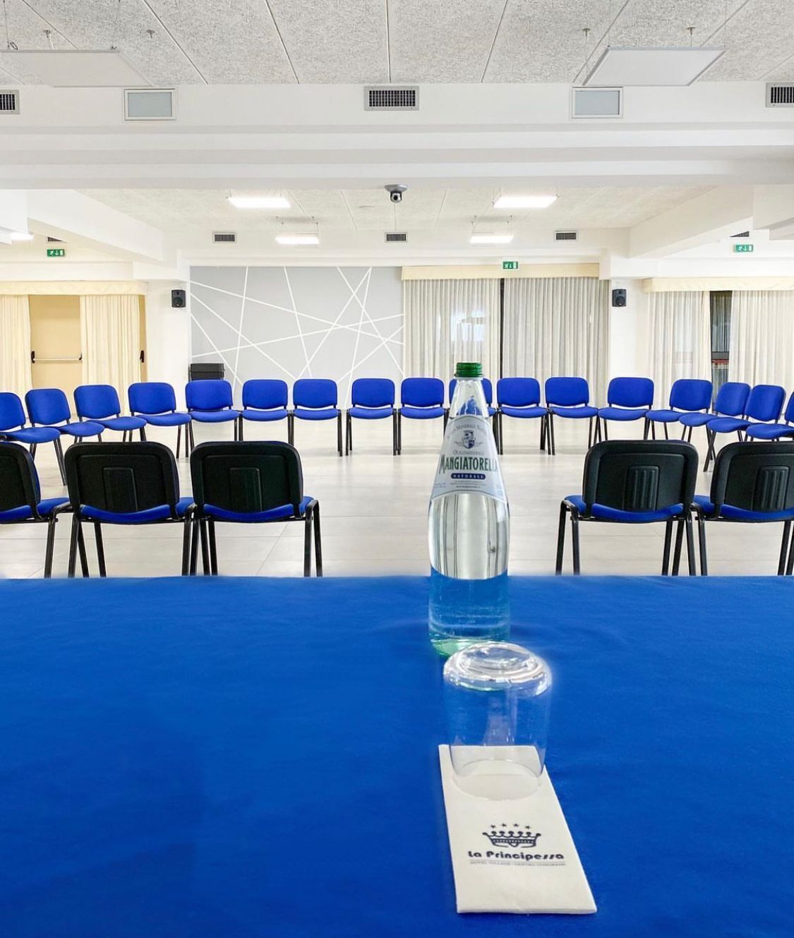 A conference room with a blue table, chairs, and a bottle of water.