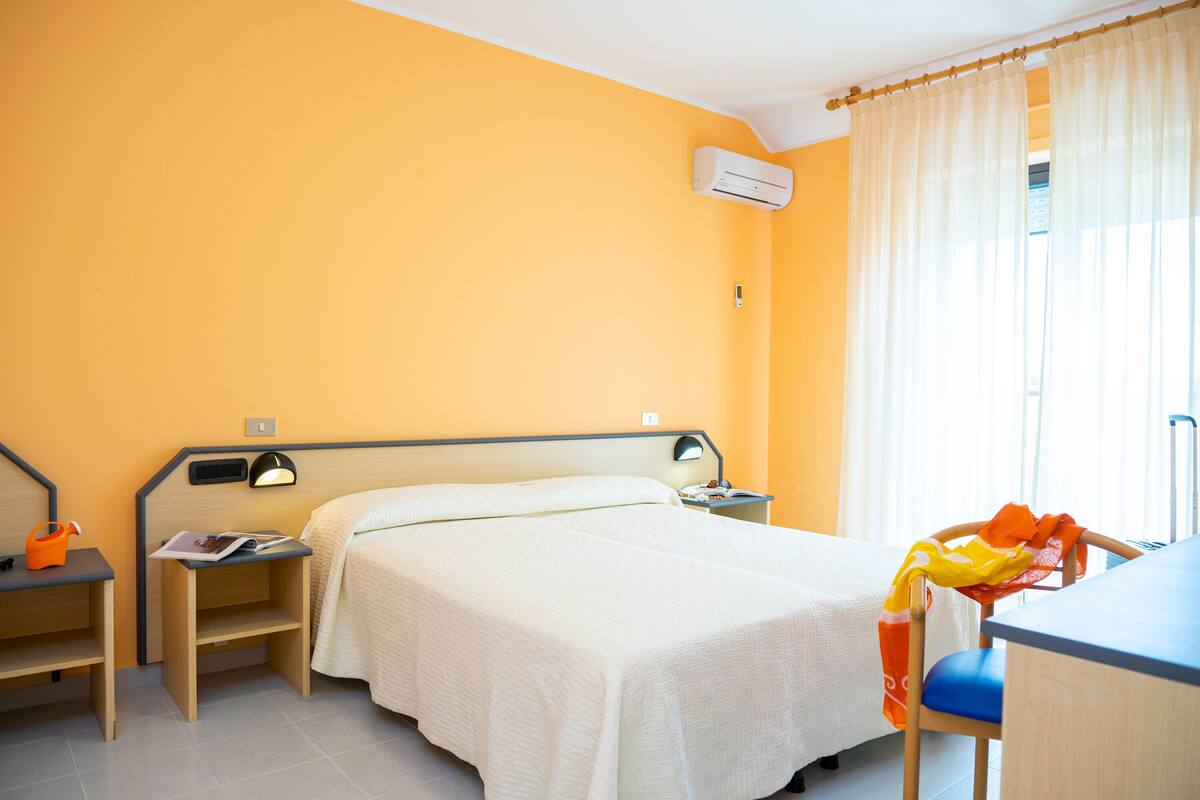 Een hotelkamer met een bed, nachtkastjes, een bureau en een airconditioning.
