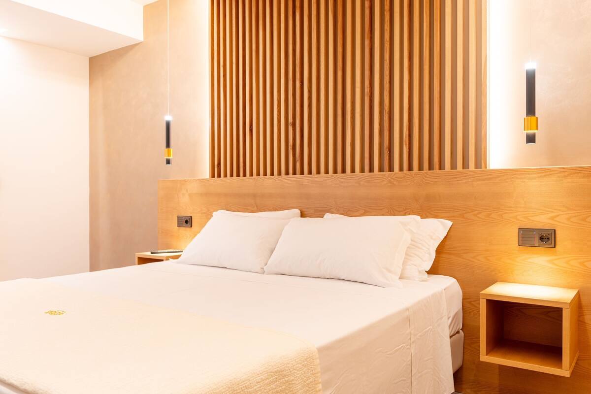 Een moderne hotelkamer met een groot bed, een houten hoofdbord, nachtkastjes en ingebouwde verlichting.