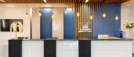 A reception desk with a modern design, featuring a wooden slatted ceiling and hanging light fixtures.