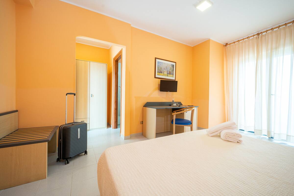 Een hotelkamer met een bed, een bureau, een stoel, een televisie en een koffer.