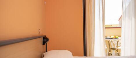 Una habitación de hotel con cama, mesita de noche y ventana con cortinas.