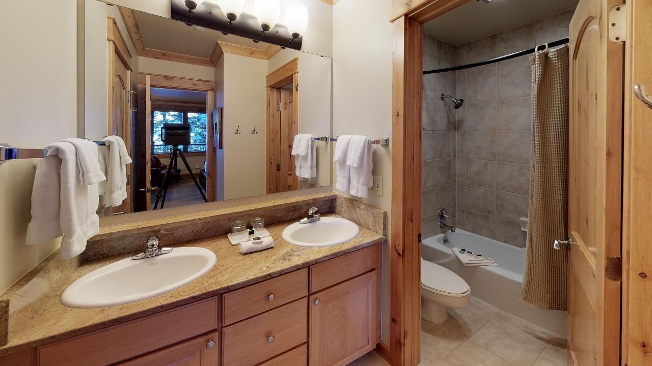 A bathroom with a double sink vanity, a large mirror, a shower area, and a toilet.