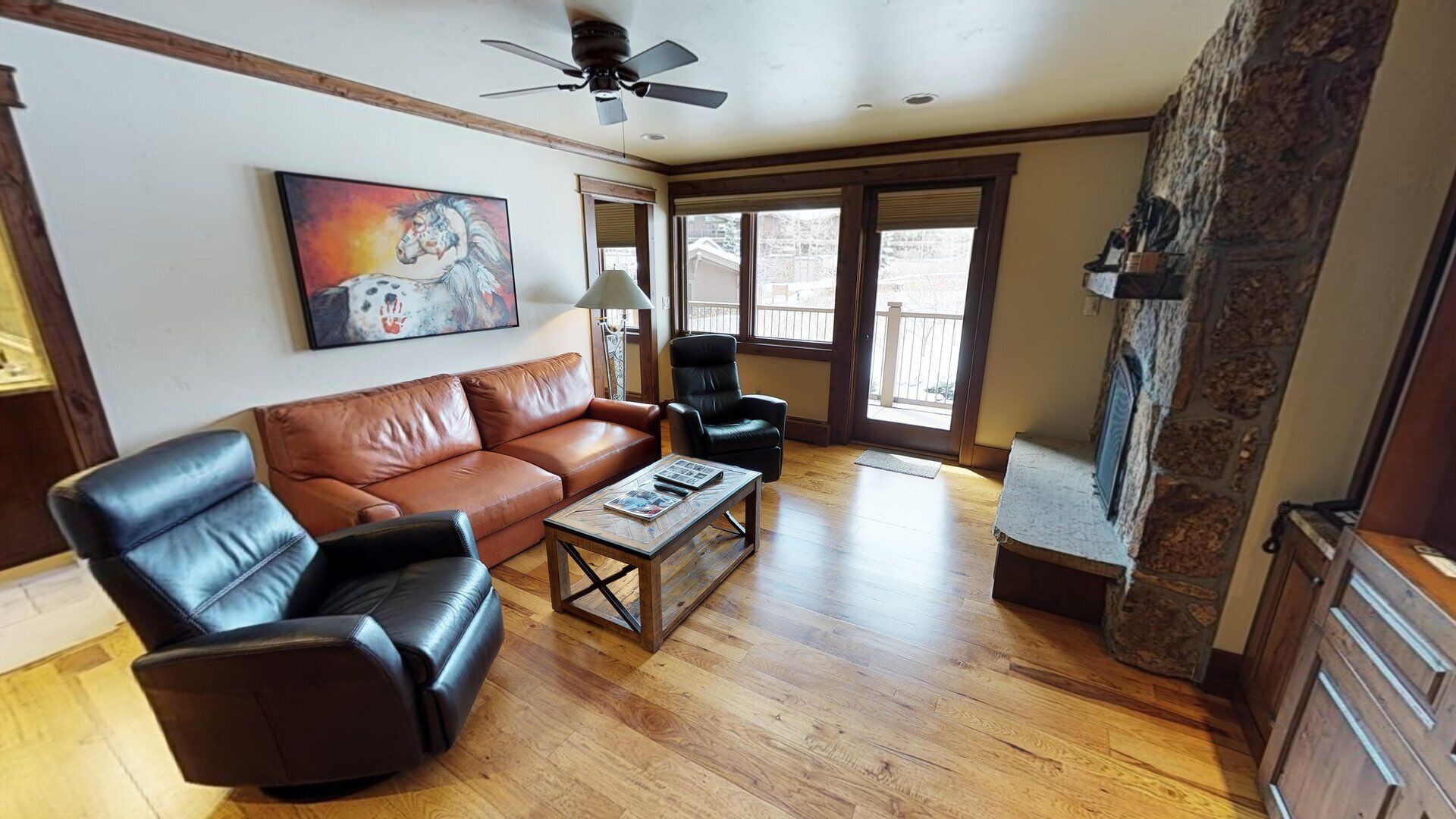 A living room with a brown leather sofa, a black leather armchair, a coffee table with magazines, a fireplace, and a painting on the wall.