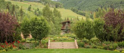 A mountain landscape with a wooden staircase leading to a building surrounded by lush greenery and trees.