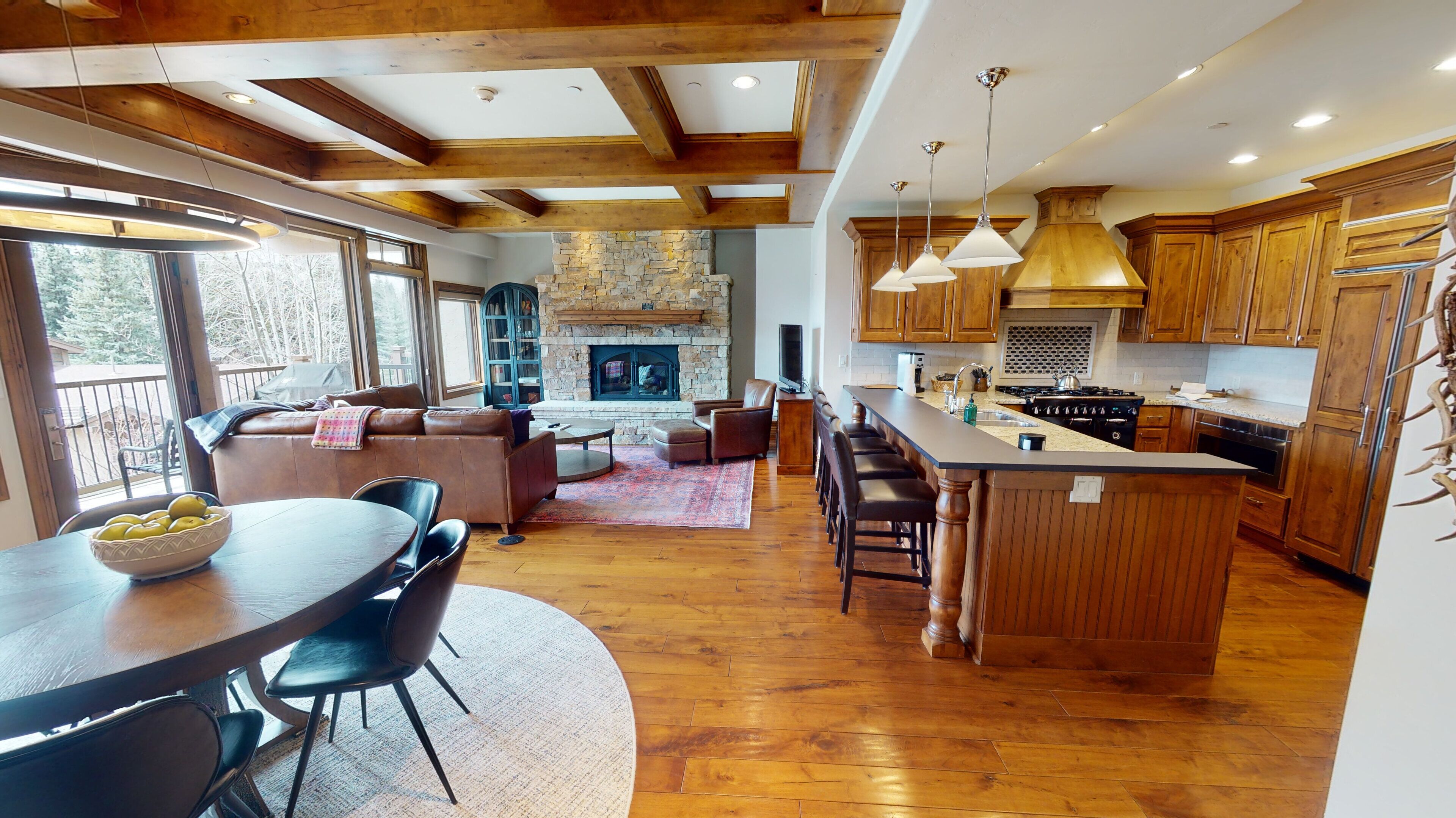 A spacious kitchen with wooden cabinets and a stone fireplace, a dining area with a round table and chairs, and a cozy living room with a fireplace and comfortable seating.