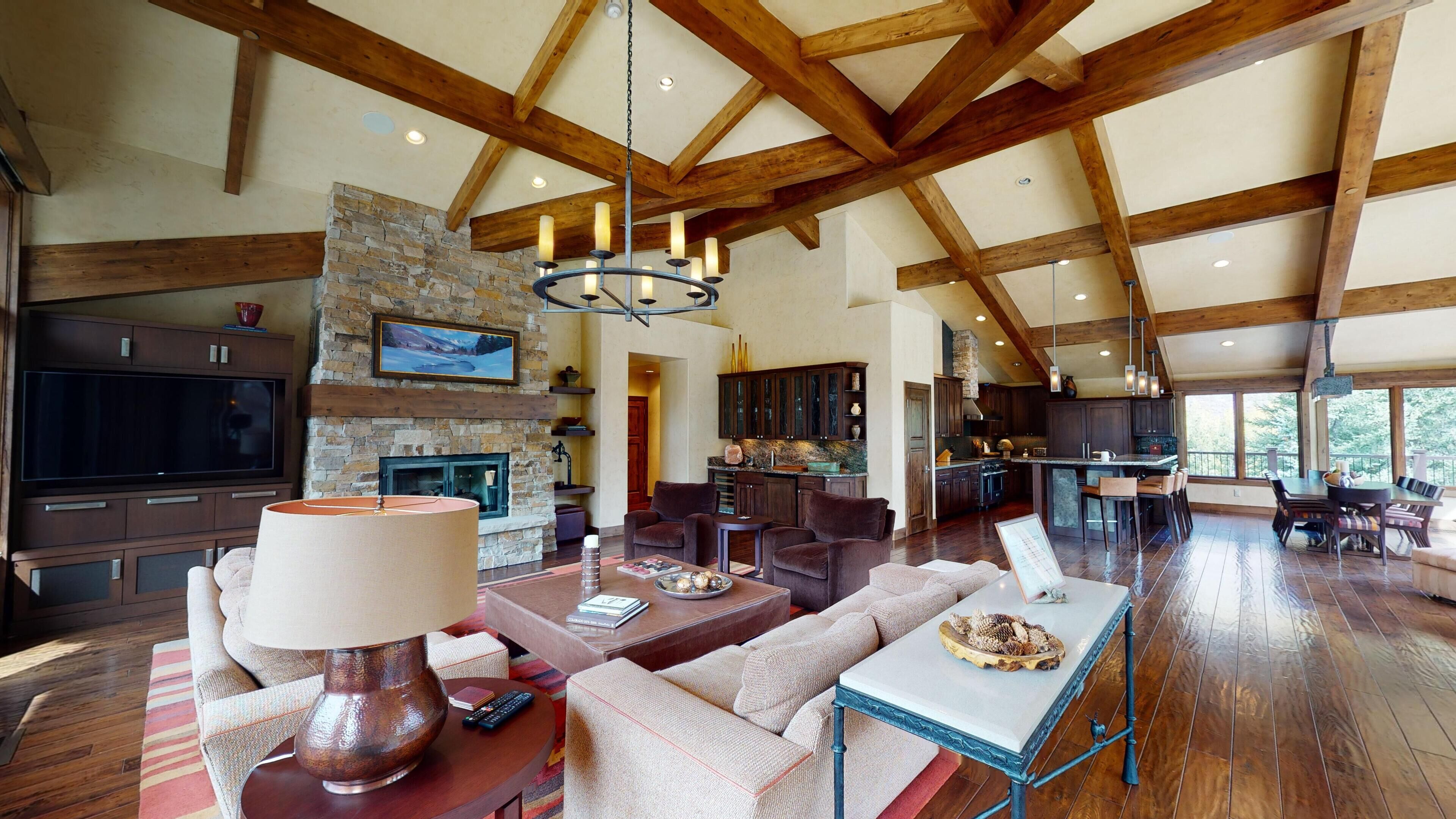 A spacious living area with a fireplace, wooden beams, a stone wall, and a large TV.