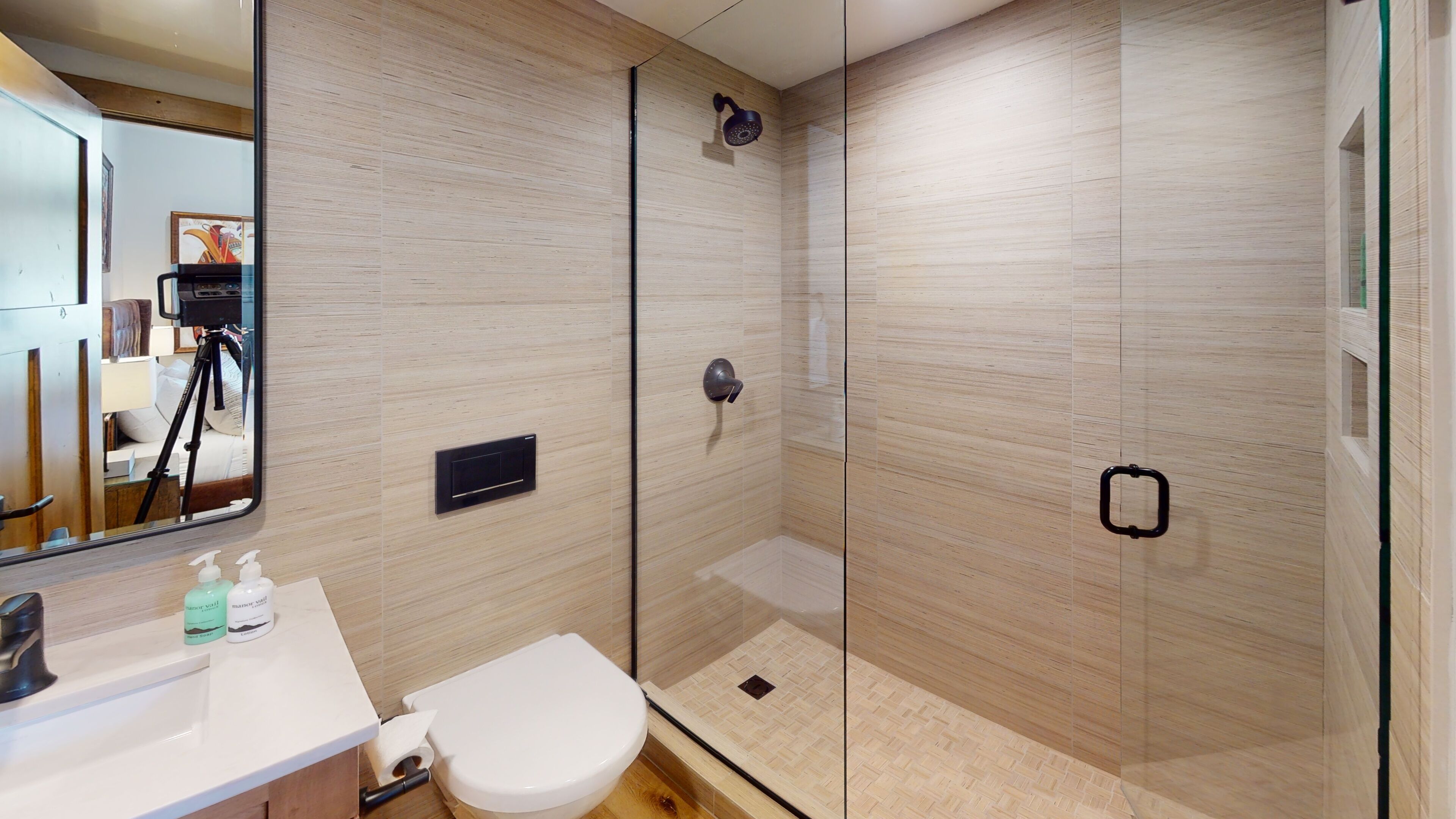Un baño moderno con cabina de ducha de vidrio, inodoro blanco y tocador con espejo.