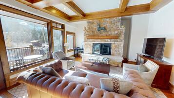 A cozy living room with a stone fireplace, comfortable seating, and large windows offering a view of the outdoors.