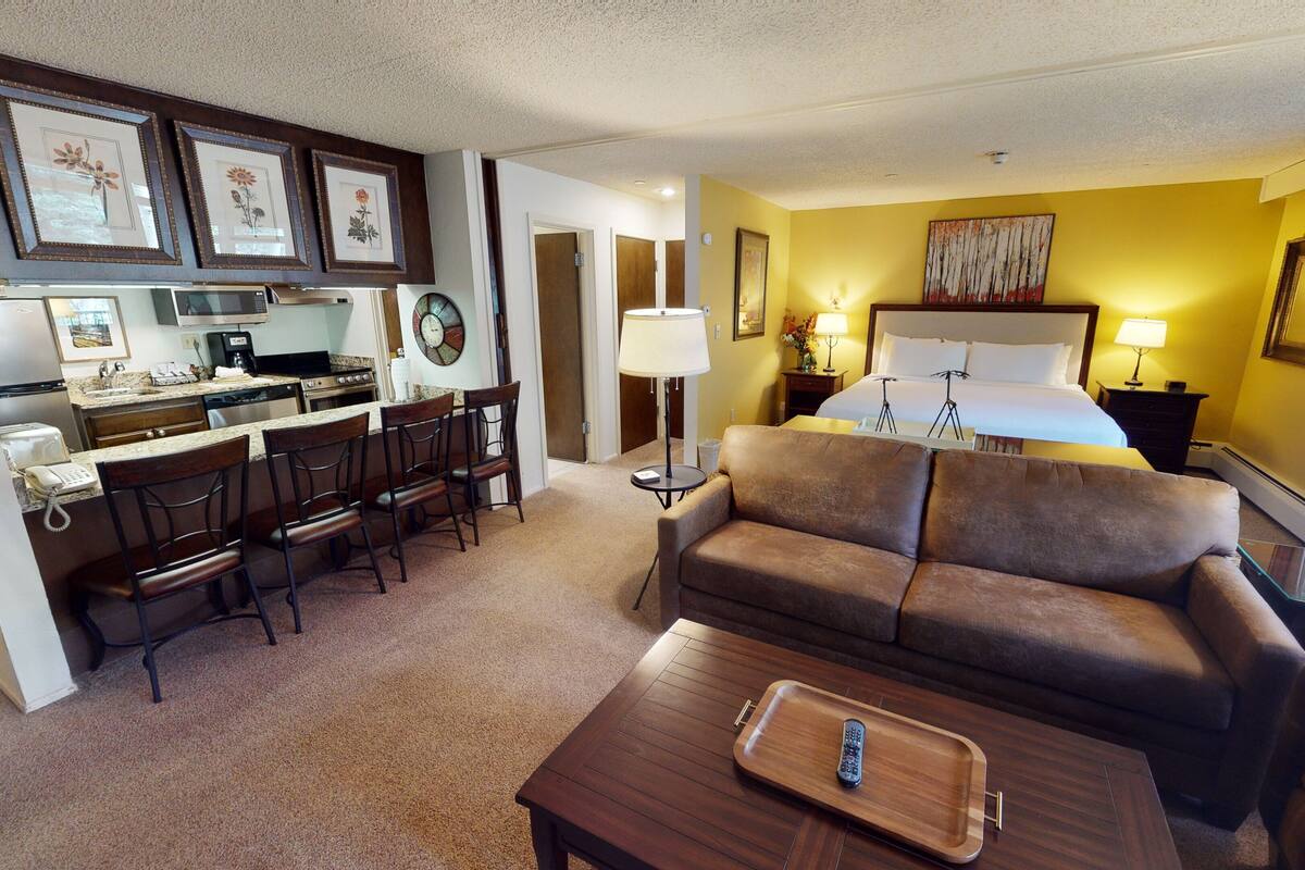 Habitación de hotel con kitchenette, sofá, zona de comedor y cama.
